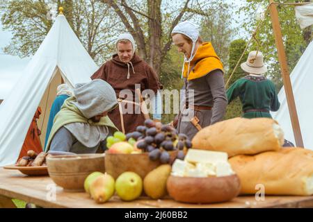 Freunde sprechen an einem Tisch mit Speisen bei einer Nachstellung eines mittelalterlichen Lagers auf dem Gelände von Tamworth Castle, England, Großbritannien. Stockfoto