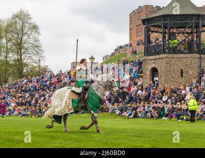 Eine in historischen Kostümen gekleidete Ritterin trägt einen Speer, während sie bei einer mittelalterlichen Nachstellung auf einem Pferd reitet. Stockfoto