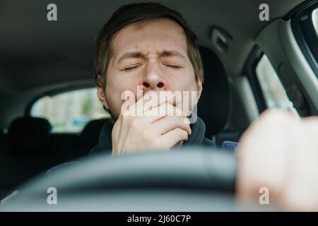 Nahaufnahme Porträt ein junger Mann, der auf dem Vordersitz des Autos gähnt. Stockfoto