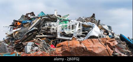 Nahaufnahme eines gemischten Schrottstapels im Schrottplatz auf einem Hintergrund mit blauem Himmel. Farbiges Durcheinander von Eisenabfällen wie alte Karosserie, Drahtgeflecht oder rostiges Blech. Stockfoto