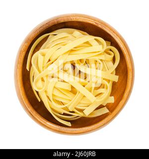 Ungekochte, getrocknete Tagliatelle-Pasta in einer Holzschüssel. Traditionelle Eiernudeln aus den Regionen Emilia-Romagna und Marken in Italien. Stockfoto