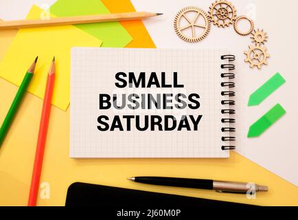 Text Small Business Saturday in Notebook auf weißem Tisch mit Office-Tools Stockfoto