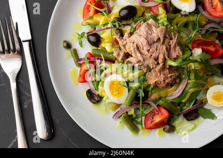 Französischer Salat Nicoise mit Thunfisch, Ei, grünen Bohnen, Tomaten, Oliven, Salat, Zwiebeln und Sardellen auf grauem Grund. Gesunde Ernährung. Stockfoto