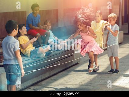 Peruanische kleine Mädchen springen Spiel von Gummiband mit europäischen Freunden Stockfoto