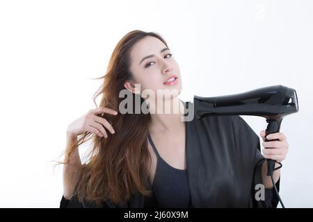 Junge und schöne chinesische Frau mit einem Haartrockner, um Haare zu trocknen, auf weißem Hintergrund - Stock Foto Stockfoto
