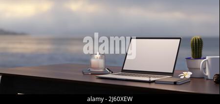 Nahaufnahme, moderner Arbeitsbereich mit Zubehör und weißer Laptop-Leinwand auf dem Tisch vor verschwommener Sicht auf Meer und Himmel im Hintergrund. 3D rende Stockfoto