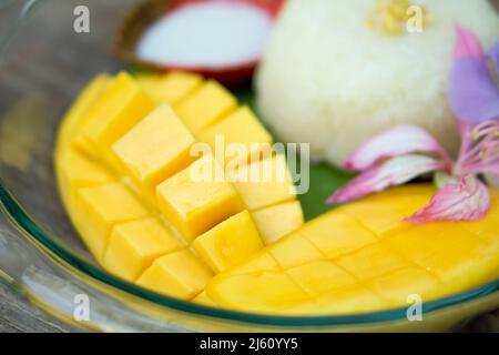 Süßer Barracuda Mango auf Bananenblättern serviert mit klebrigem Reis und Kokosmilch, die mit rosa Blüten verziert ist. Stockfoto