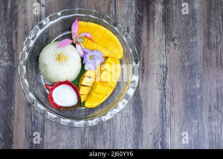 Süßer Barracuda Mango auf Bananenblättern serviert mit klebrigem Reis und Kokosmilch, die mit tropischen Blumen verziert ist. Draufsicht Stockfoto