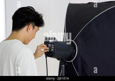 Asiatischer Fotograf, der die Helligkeit der Lichter für die Aufnahme von Models im Studio anpasst. Stockfoto