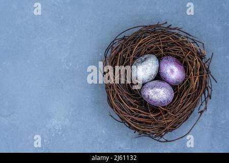 Osterfarbige Eier in einem Nest, in einem Korb. Schöne gruppierte blaue und graue Ostereier mit Wachteleiern auf dunklem Hintergrund. Hochwertige Fotos Stockfoto