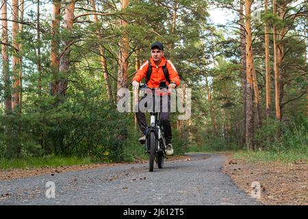 Ein Biker, der durch einen Pfad zwischen den Bäumen im Wald reitet. Aktiver Zeitvertreib. Sporthobby. Ein Mann auf einem Elektrofahrrad im Park. Stockfoto