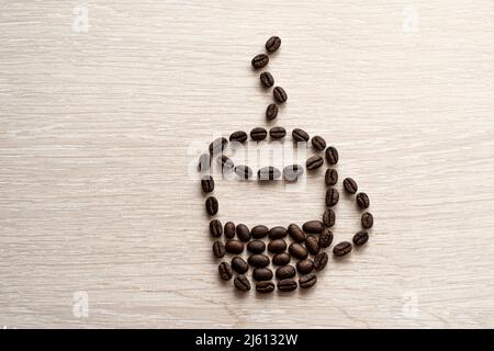 Kaffeetasse aus Bohnen auf weißem Hintergrund. Kaffeebohne Nahaufnahme auf einem Holztisch. Kaffeepause, Stockfoto