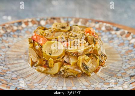 Zucchinistücke mit Tomaten auf Teller auf Holzboden Stockfoto