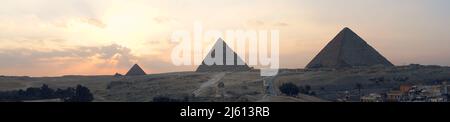 Die große Sphinx und Pyramiden unter strahlender Sonne. Panoramablick auf das Gizeh-Hochplateau mit den großen Pyramiden und der Sphinx am Abend bei Sonnenuntergang Stockfoto