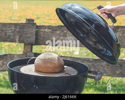 Wie man Brot im Garten mit einem Holzkohlegrill im Garten mit schönem Gartenzaun im Hintergrund backen kann Stockfoto