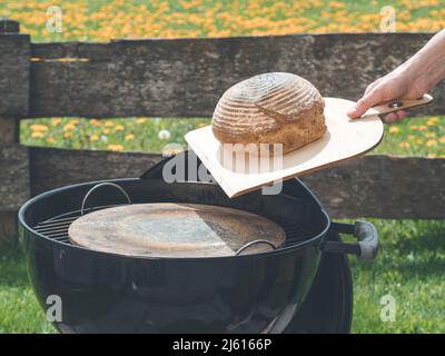 Mit einer Pizzaschaufel, um das hausgemachte Brot aus heißem Pizzastein im Garten mit einem bbq-Grill zu übertragen Stockfoto