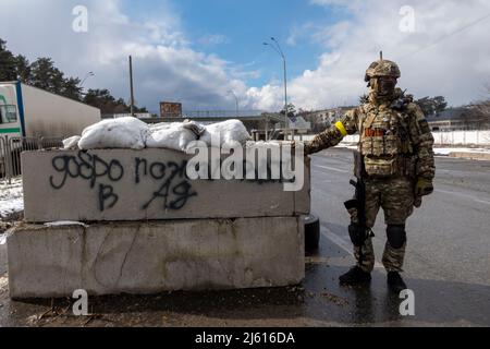 BROVARY, UKRAINE 08. März. Ein bewaffneter ukrainischer Militärangehöriger steht an einer Betonbarrikade mit der Aufschrift „Willkommen zur Hölle“ an einem Kontrollpunkt in der Stadt Brovary außerhalb von Kiew am 08. März 2022 in Brovary, Ukraine. Russland begann eine militärische Invasion der Ukraine, nachdem das russische parlament Verträge mit zwei abtrünnigen Regionen in der Ostukraine gebilligt hatte. Es ist der größte militärische Konflikt in Europa seit dem Zweiten Weltkrieg Stockfoto