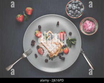 Traditionelle belgische Waffeln mit frisch gepflückten Früchten wie Erdbeeren und Blaubeeren sowie Eiscreme mit Puderzucker und Minze - topview Stockfoto