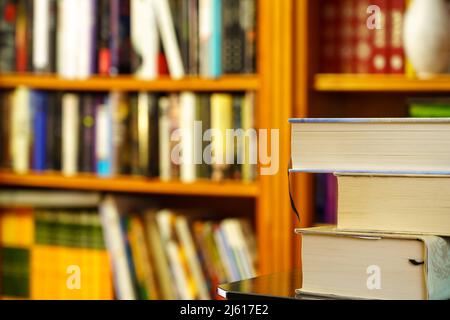 Bibliothek mit vielen Büchern zum Lesen, Computer in den Regalen. Gestapelte Bücher im Vordergrund. Speicherplatz kopieren. Hintergrund. Stockfoto