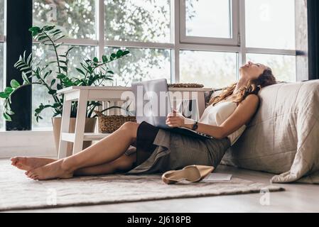 Das müde Mädchen sitzt auf dem Boden des Schlafzimmers und lehnt sich zurück auf das Bett. Stockfoto