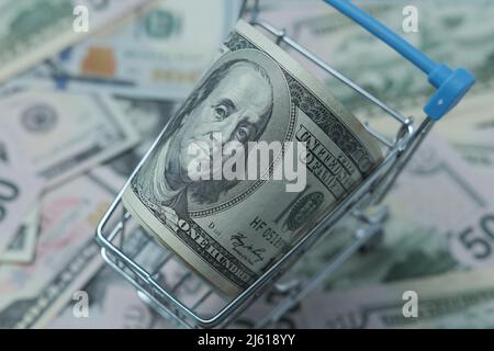 In einen Schlauch gerollte Dollars liegen in einem Einkaufskorb. Der Korb steht auf einem verschwommenen Geldhintergrund. Stockfoto