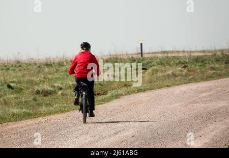 Eine Radfahrerin in einer roten Jacke, die auf einer Schotterpiste in freier Natur unterwegs ist Stockfoto