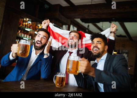 Männerfans schreien und beobachten Fußball im Fernsehen und trinken Bier in einer Kneipe Stockfoto