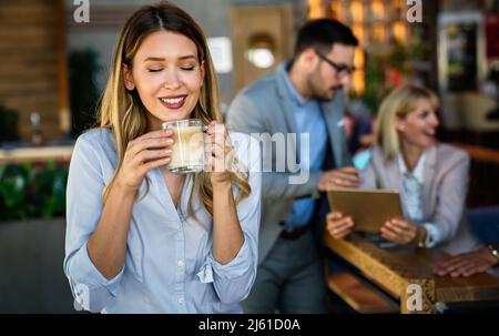 Porträt einer glücklichen jungen Geschäftsfrau, die in einer Pause Kaffee trinkt. Im Hintergrund ihre Kollegen Stockfoto