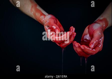 Frauenhände in einer zähflüssigen roten Flüssigkeit ähnlich dem Blut. Stockfoto