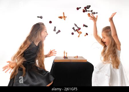 Kleine Mädchen Schwestern spielen Schach auf weißem Hintergrund. Sport- und Hobbykonzept. Kognitive Entwicklung. Intellektuelles Spiel. Intelligente Kinder. Stockfoto