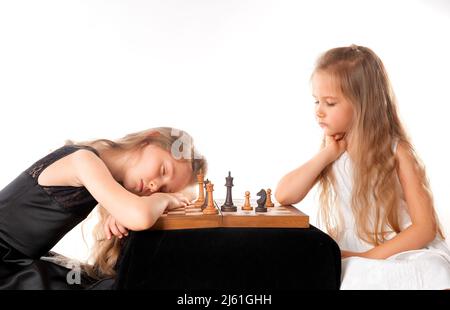 Kleine Mädchen Schwestern spielen Schach auf weißem Hintergrund. Sport- und Hobbykonzept. Kognitive Entwicklung. Intellektuelles Spiel. Intelligente Kinder. Stockfoto