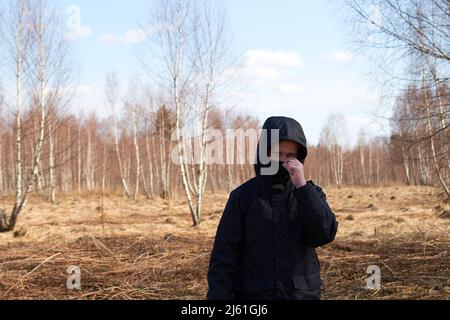 Ein europäischer Teenager in einer schwarzen Kapuzenjacke und einer schwarzen Maske Stockfoto