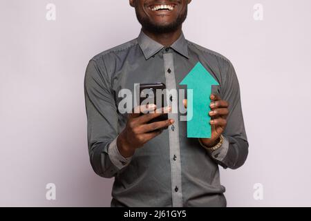 Aufgeregter afrikanischer Mann, der Telefon und Pfeil nach oben hält Stockfoto