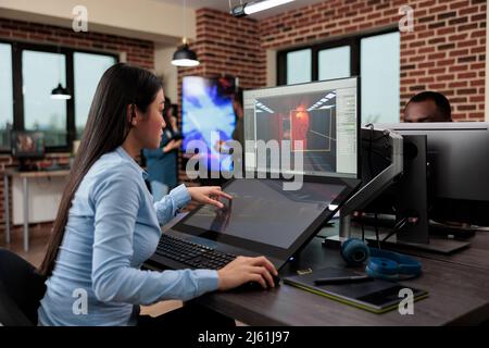 Kreative Firma Spiel Entwickler sitzen in der Produktionsabteilung während der Entwicklung von 3D Videospielen Szenen und Umgebung. Asiatischer Mitarbeiter, der mit moderner Software auf Level-Design arbeitet. Stockfoto