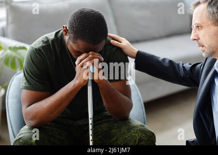 Reifer Psychologe tröstet und unterstützt Black Soldier bei der Behandlung von PTSD bei der Therapiesitzung Stockfoto