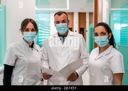 Arzt und Krankenschwestern, die Gesichtsschutzmasken tragen, stehen im Korridor des Krankenhauses Stockfoto