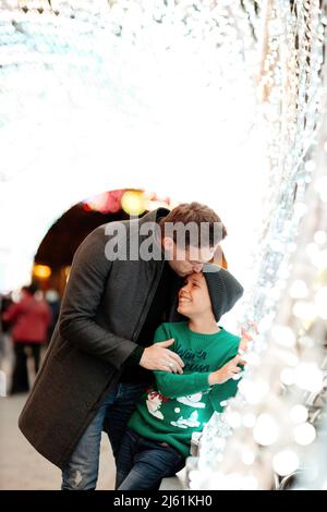 Vater küsst Sohn im Tunnel mit Weihnachtsbeleuchtung Stockfoto