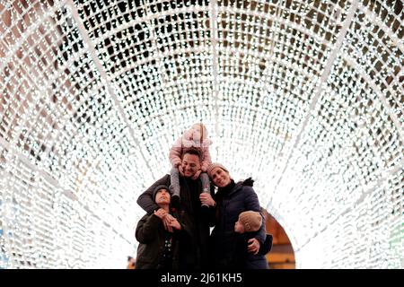 Glücklicher Vater, der seine Tochter auf den Schultern trägt und mit seiner Familie im beleuchteten Tunnel steht Stockfoto