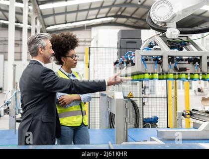 Geschäftsmann im Gespräch mit Ingenieur über Roboterarmmaschine in der Fabrik Stockfoto