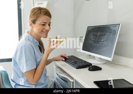 Lächelnder Zahnarzt, der über Lautsprecher in der Zahnklinik auf dem Mobiltelefon spricht Stockfoto