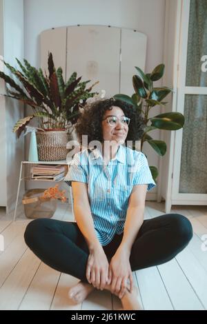 Nachdenkliche Frau mit Brillen, die zu Hause auf dem Dielenbrett sitzt Stockfoto