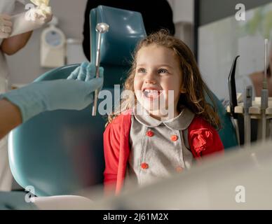 Nettes kleines Mädchen, das in der Klinik auf dem Zahnarztstuhl sitzt Stockfoto