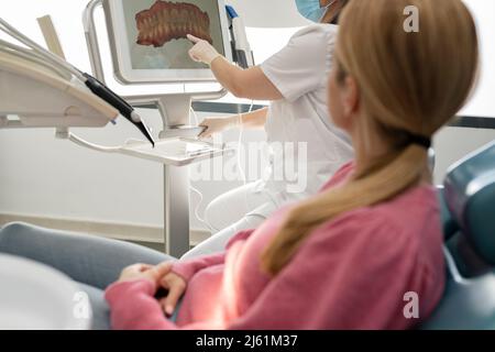 Zahnarzt erklärt dem Patienten in der Zahnklinik das Bild der Zähne auf dem Computerbildschirm Stockfoto