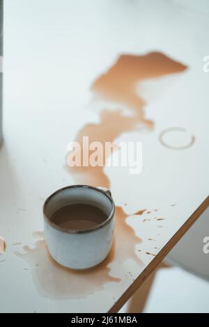 Verschüttete Tasse Kaffee auf dem Tisch zu Hause Stockfoto