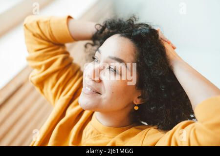 Lächelnde Frau, die mit den Händen hinter dem Kopf sitzt Stockfoto