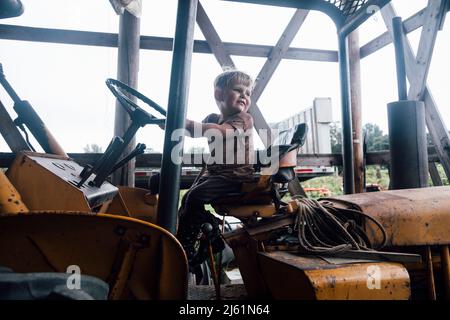 Vorschuljunge sitzt auf dem Traktor auf dem Bauernhof Stockfoto