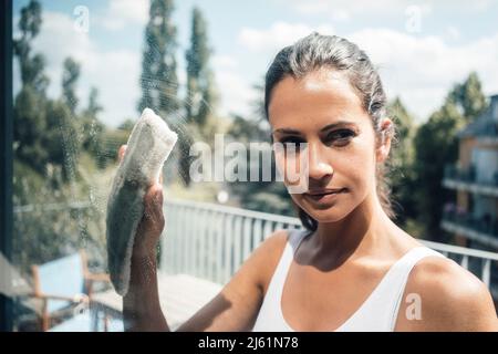 Frau putzt Glasfenster an sonnigen Tagen Stockfoto