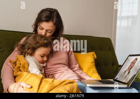 Mutter umarmt kranke Tochter Beratung Arzt online über Laptop zu Hause Stockfoto