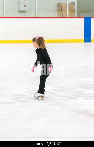 Kleine Mädchen, die Eiskunstlauf üben, bewegen sich auf der Indoor-Eisbahn. Stockfoto