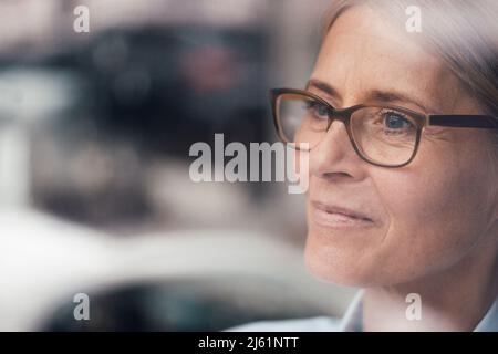 Nachdenkliche reife Frau durch Glas gesehen Stockfoto